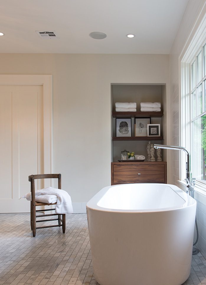 Custom walnut storage space and shelves occupy a nook in the master bath. A chair and bathroom accessories were provided by Fifteenth and Home. Photo by Nathan Harmon.