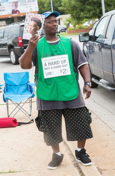 A Curbside Chronicle Vendor Shows off the publication’s latest issue. Photo by Brent Fuchs. 